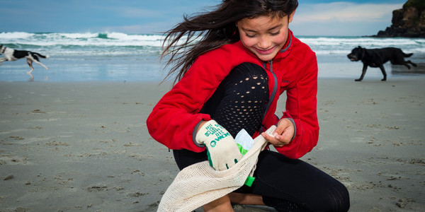 A young girl crouching on a beach, wearing a glove, and picking up plastic.