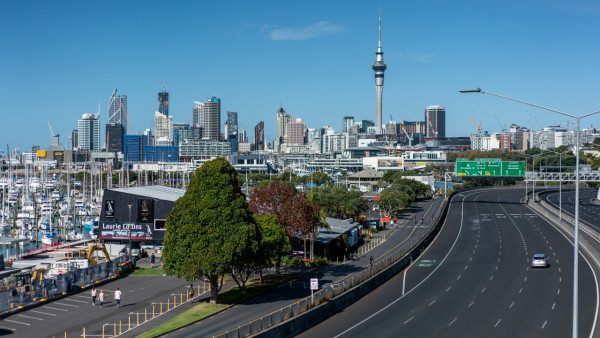 One car on a five-lane motorway in Auckland with tall modern buildings and the Sky Tower behind.