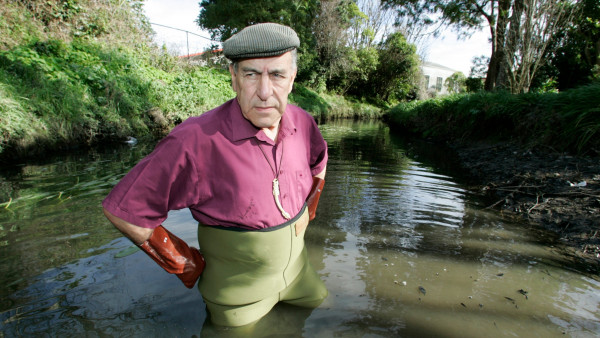 A man wearing a cap, waders and rubber gloves stands in thigh-deep muddy water.