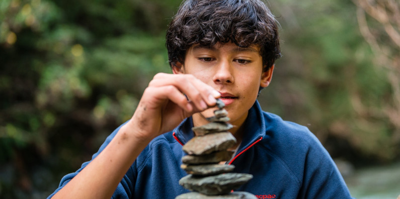 A teenager stacking rocks on top of each other.