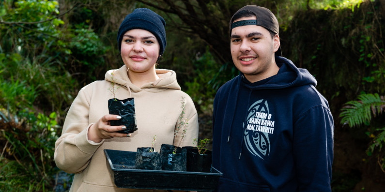 Two people holding a tray filled with saplings ready to be planted at Hicks Bay.