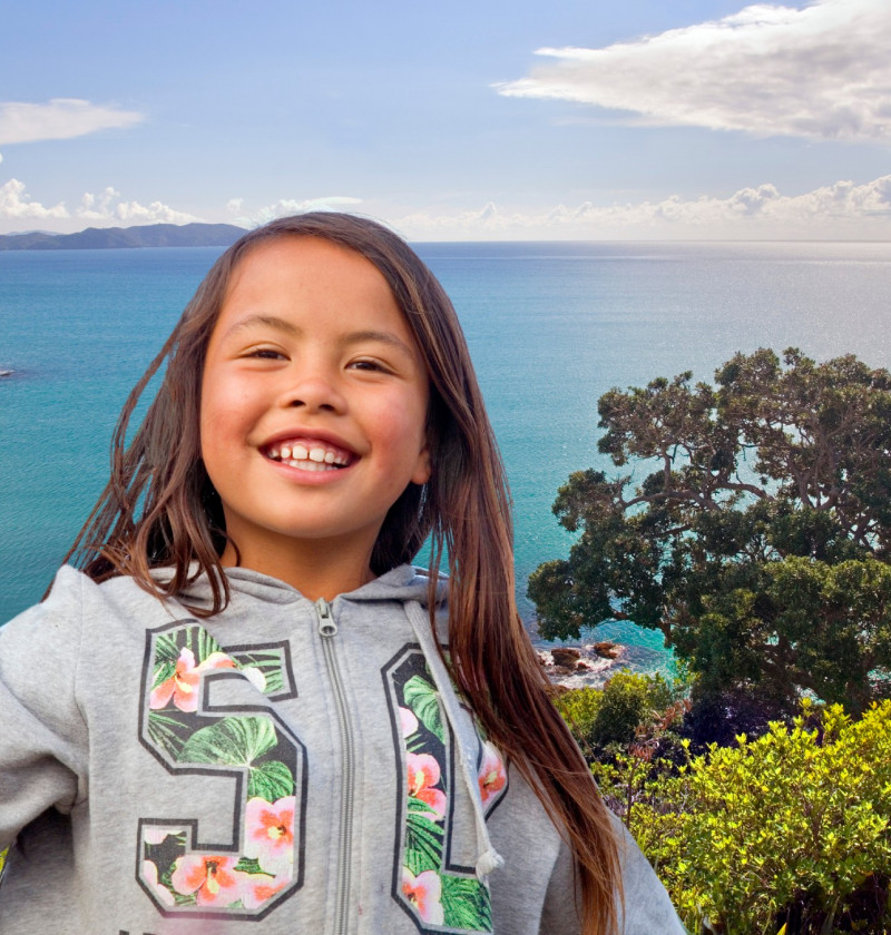 A girl smiles in the foreground with a view of the bay behind. 