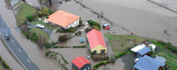 Brown floodwater reaches up to five houses and covers a road and large paddocks.