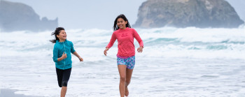 Two girls run through the waves at a wild beach. 