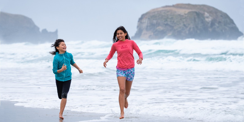Two girls run through the waves at a wild beach. 