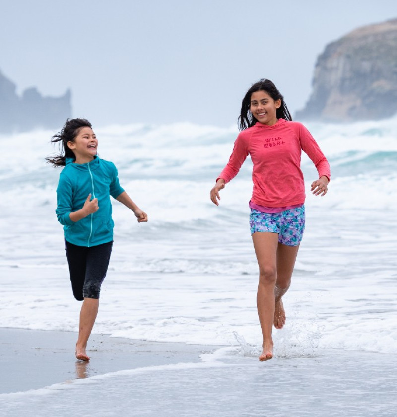 Two girls run through the waves at a wild beach. 