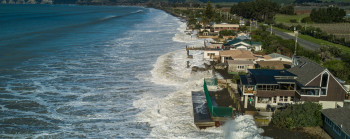A coastline with a line of houses being breached and flooded by the ocean.