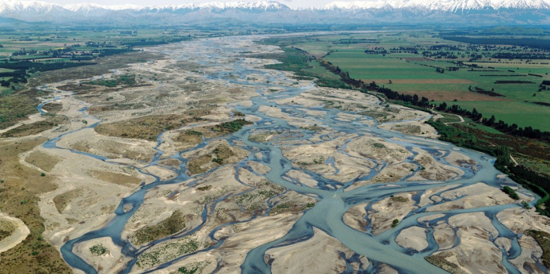 A braided river reaching into the distance towards the mountains with nearby farmland.