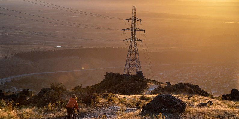 A person mountain biking at sunrise. A large electricity pylon with wires is at the centre of the image.