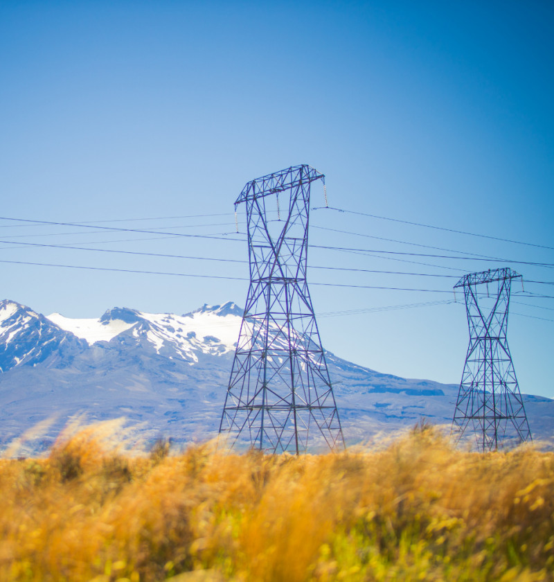 An electricity transmission pylon with a mountain range in the background and desert plans in the foreground.  