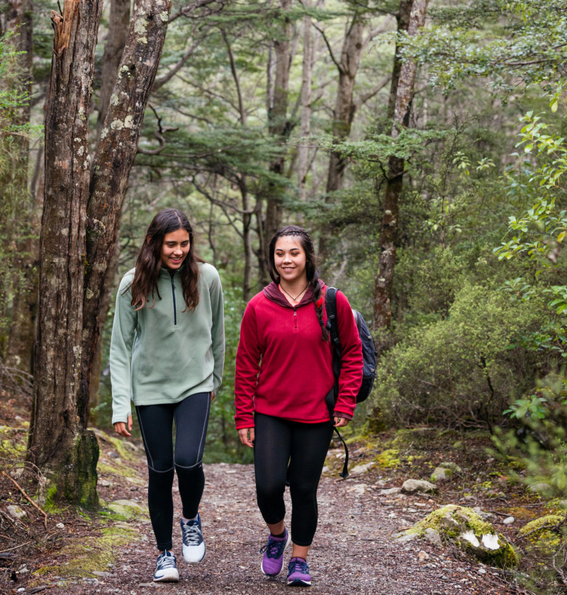 Two teenage girls walking on a track in a native forest.  