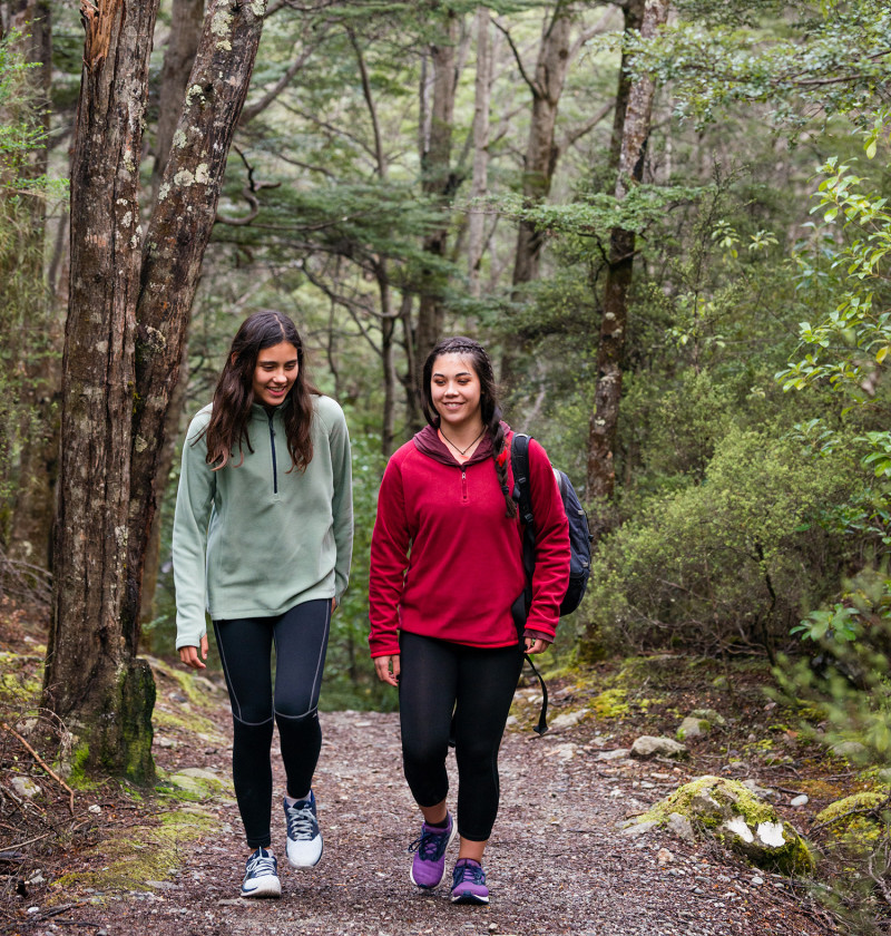 Two young people smile and walk along a track in a native forest.