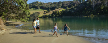 Two adults and two children walk along the sandy bank of a river.