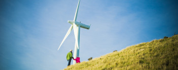 Two people stand by a wind turbine on a hill.