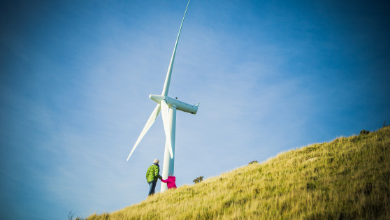 Two people stand by a wind turbine on a hill.