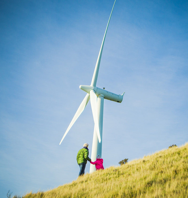 Two people stand by a wind turbine on a hill.