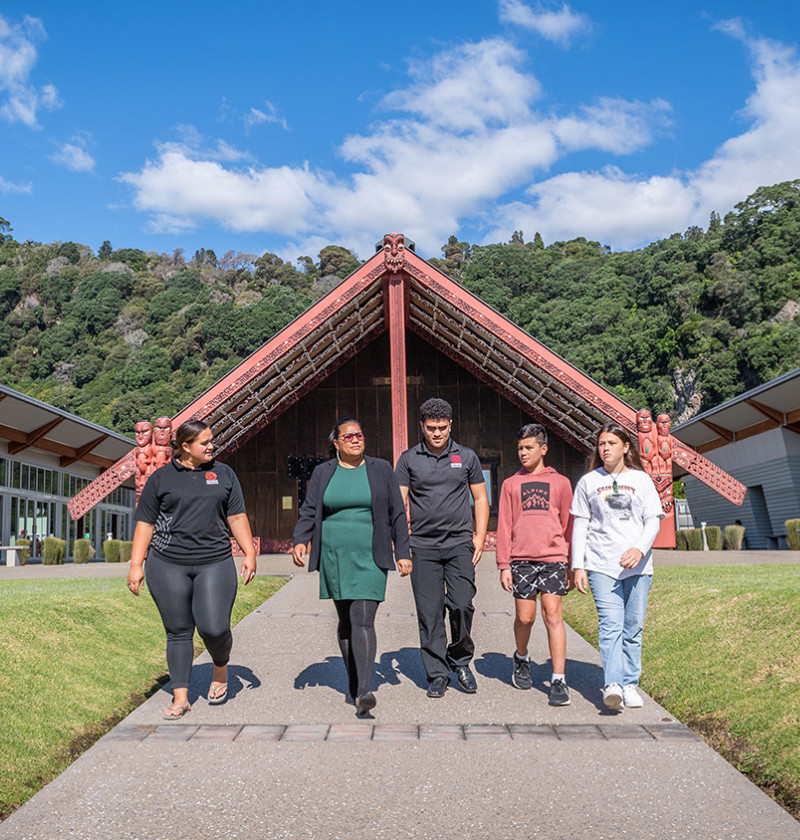 A group of people walking along a path in front of a marae.  