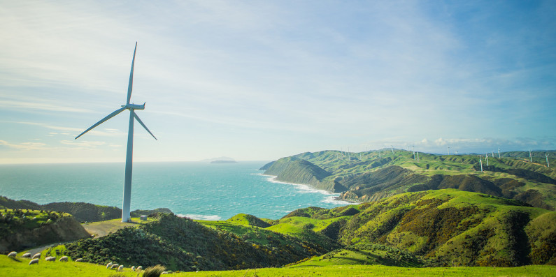 A wind turbine on farmland with the ocean in the background.  