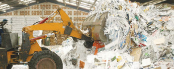 A digger grabbing at tall piles of paper-based waste.