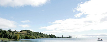A blue sky with clouds, above a still body of water.