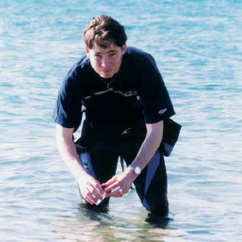 A man standing knee deep in the ocean, collecting a water sample to test the water quality.
