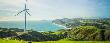 A wind turbine on farmland with the ocean in the background.  