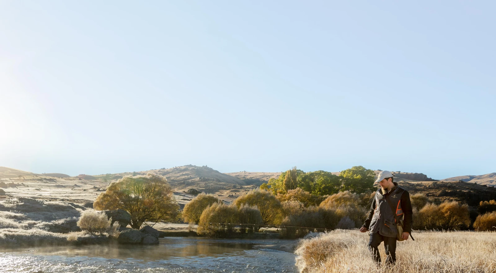 A man by the side of a river with a fishing pole.