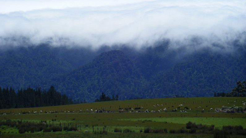 Farm in the distance surrounded by mountains and low cloud