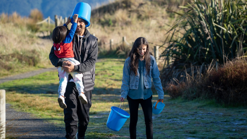 A man with his children walking and holding blue buckets