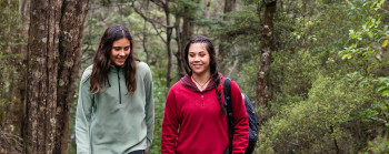 Two young people smile and walk along a track in a native forest.
