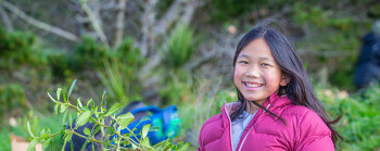 A young person smiling and holding a native plant at a tree-planting event. Photo sourced from Jeff McEwan, Capture studios.