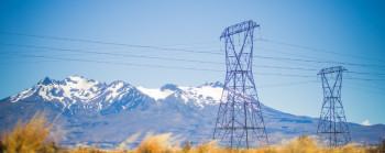 An electricity transmission pylon with a mountain range in the background and desert plans in the foreground.