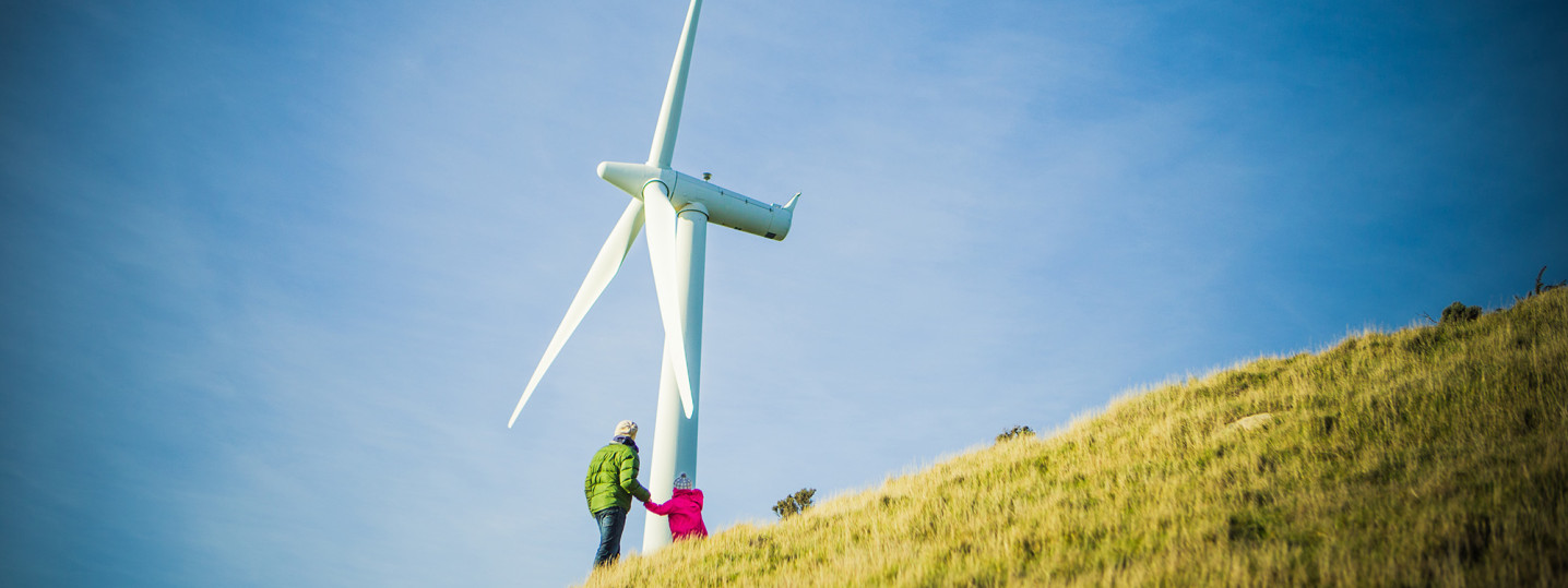 Two people stand by a wind turbine on a hill.  