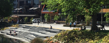 A photo showing people interacting with an urban environment in Christchurch. There are steps leading to the river and trees and other plants growing. 