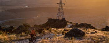A person mountain biking at sunrise. A large electricity pylon with wires is at the centre of the image.