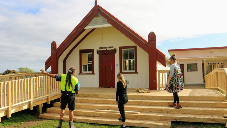 Three people standing in front of buildings on a newly constructed deck with steps and a ramp at Waipapa Marae, Waitōtara. 