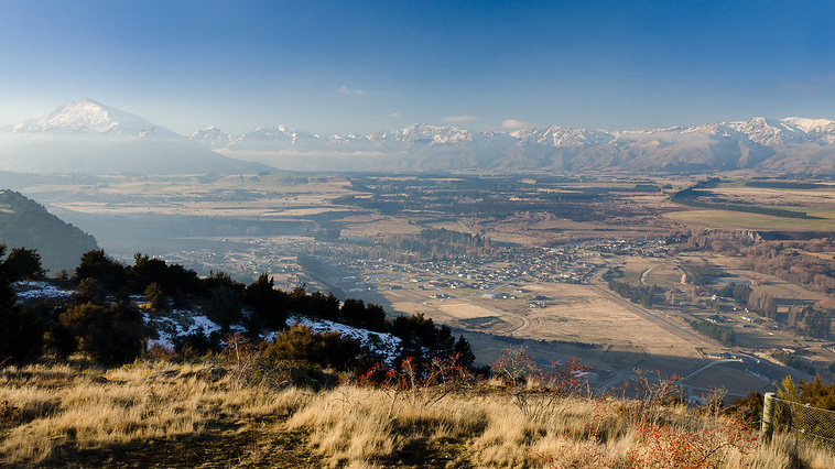 A panorama view taken from the Mt Iron summit. A township can be seen below and snow-covered hills appear in the distance. 
