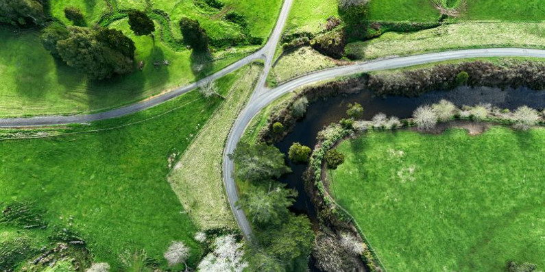 Birdeye view of green farmland with a stream and road running across it.