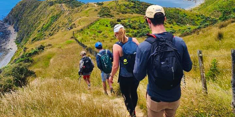 Group of four people walking down a hill towards the ocean