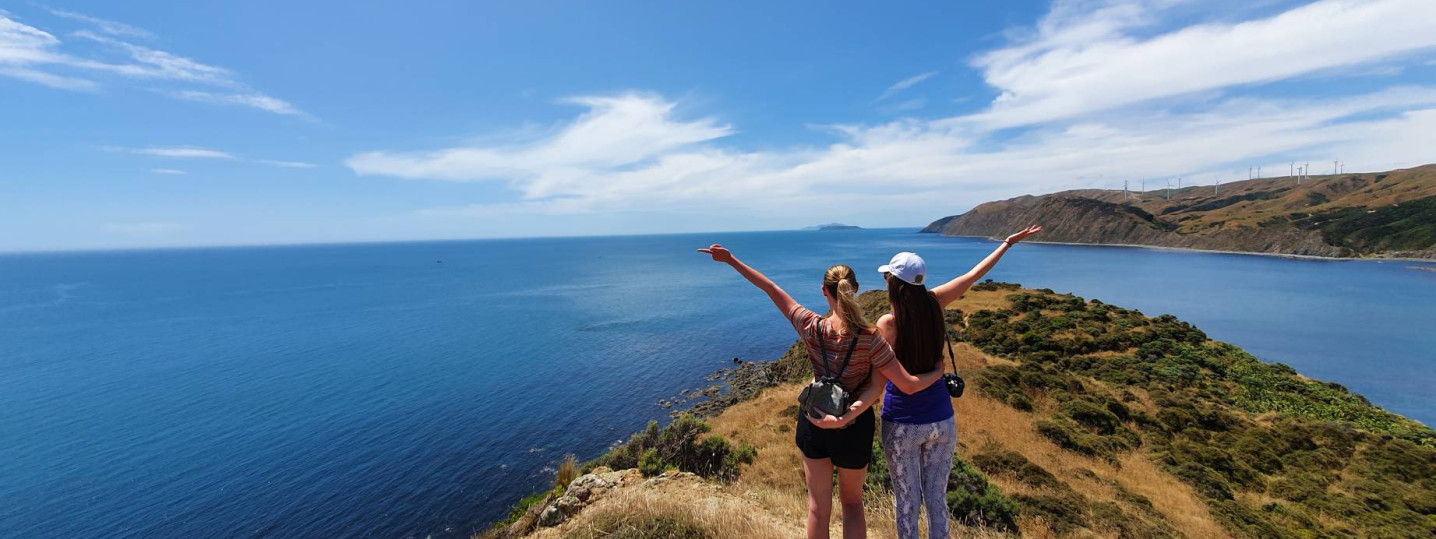 Two women standing close to the edge of a hill overlooking the ocean