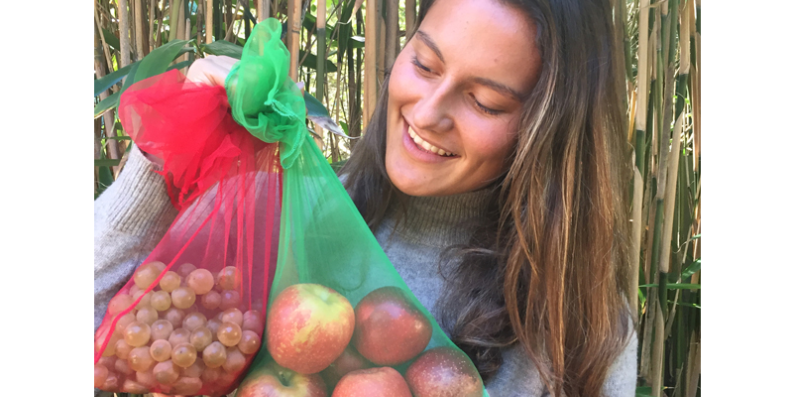 A woman holding two reusable produce bags with fruit in them.
