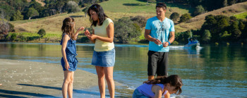 Two adults and two children look at objects they find in the shallow water of a river.