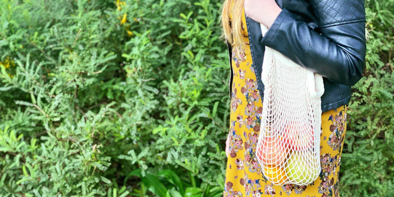 A woman carrying a reusable produce bag with different fruit in it.