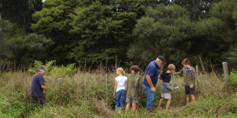 Two adults teaching kids how to build a fence to help keep predators out of the bushes.