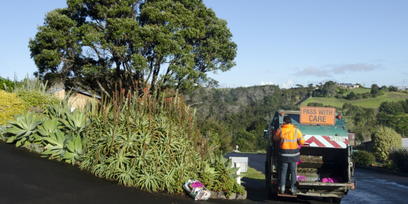 Man standing on a rubbish truck doing rubbish collection.