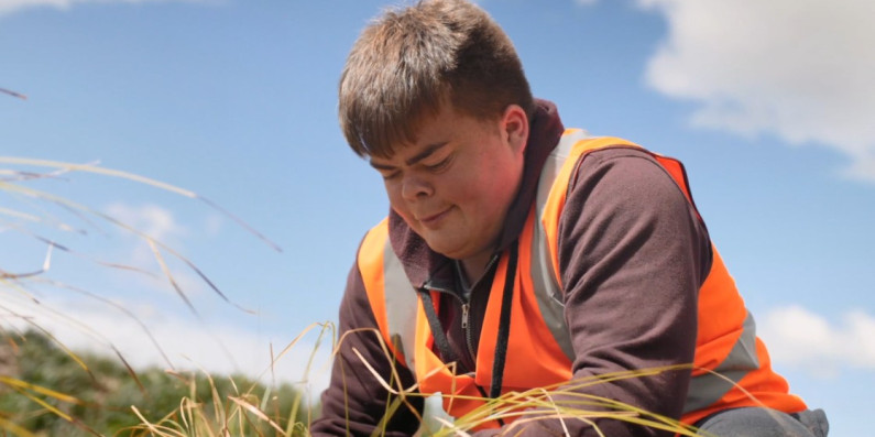 A man planting grass in a vest.
